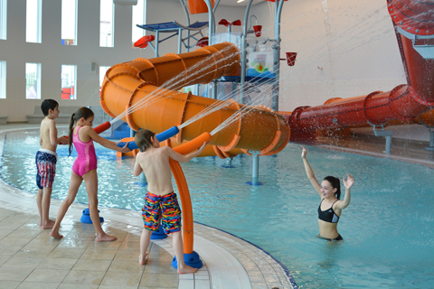 three children firing water cannons with pool and water slides in the background