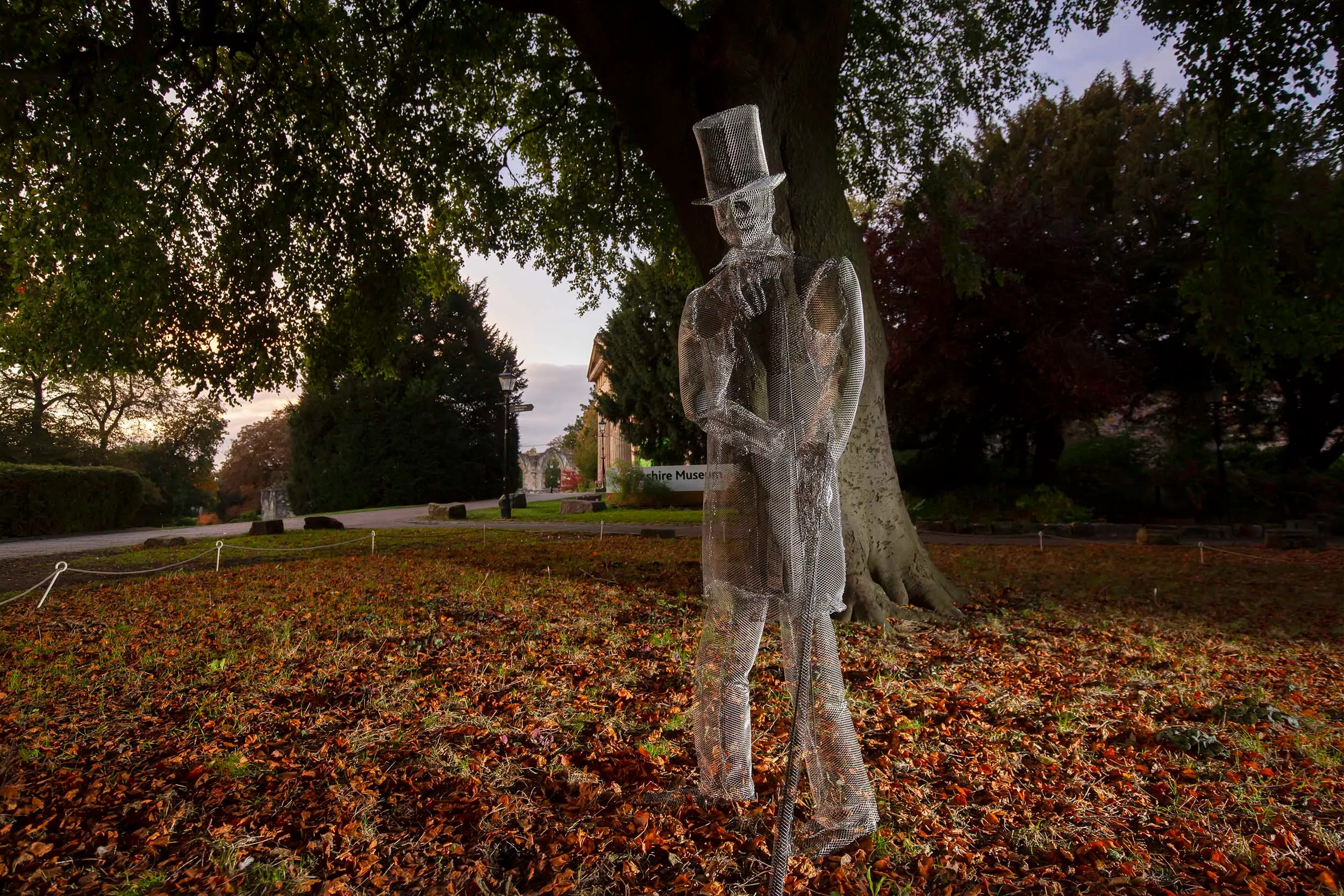 Translucent wire mesh ghost sculpture standing in an autumnal garden in York city centre