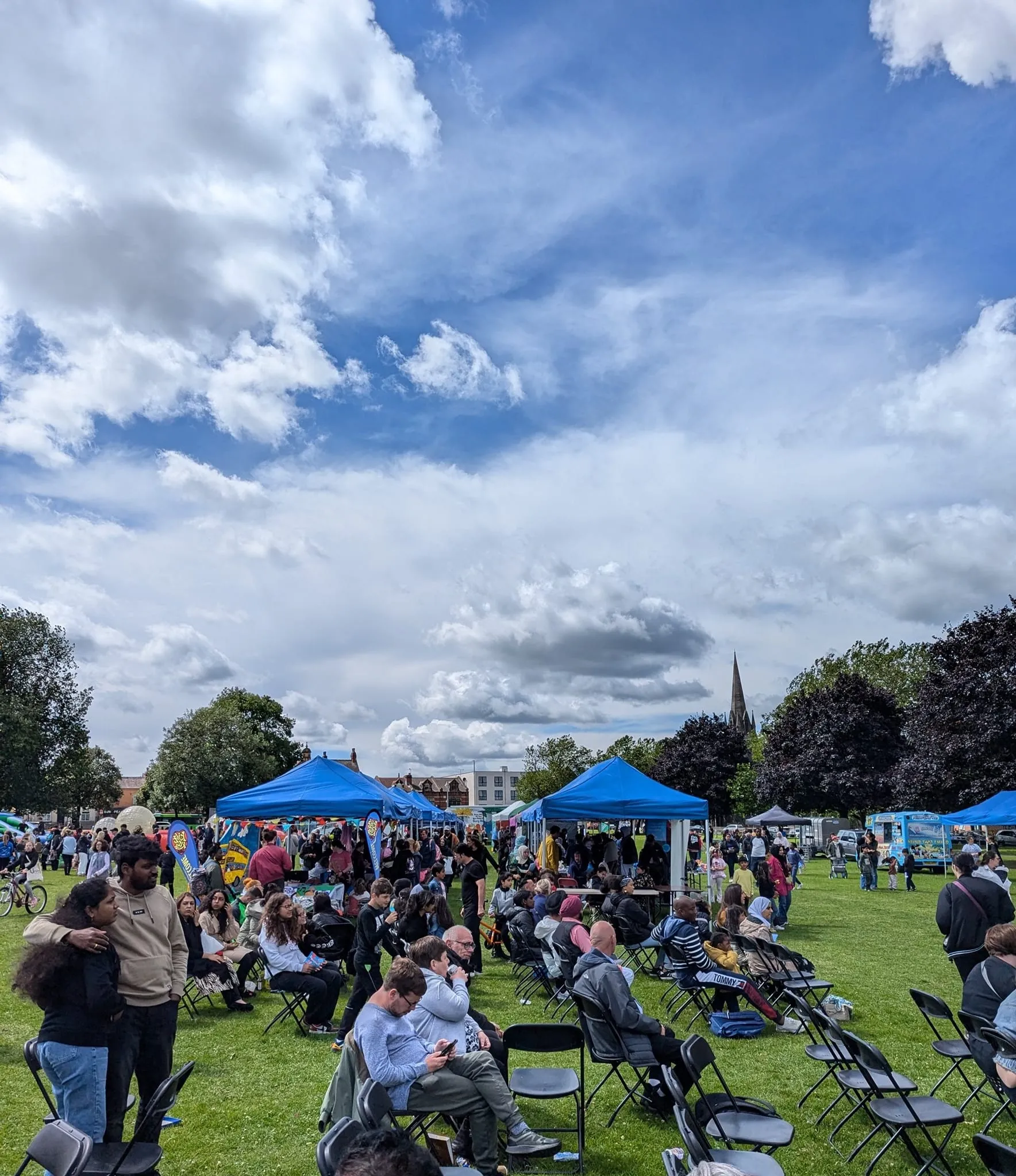 People sitting on a grassy field at Holbeck Gala with gazebo stalls in the background, the event is held in July