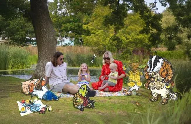 people picnicing on grass with trees behnd and illustraions of the Wind in the Willows characcters at RHS Garden Harlow Carr