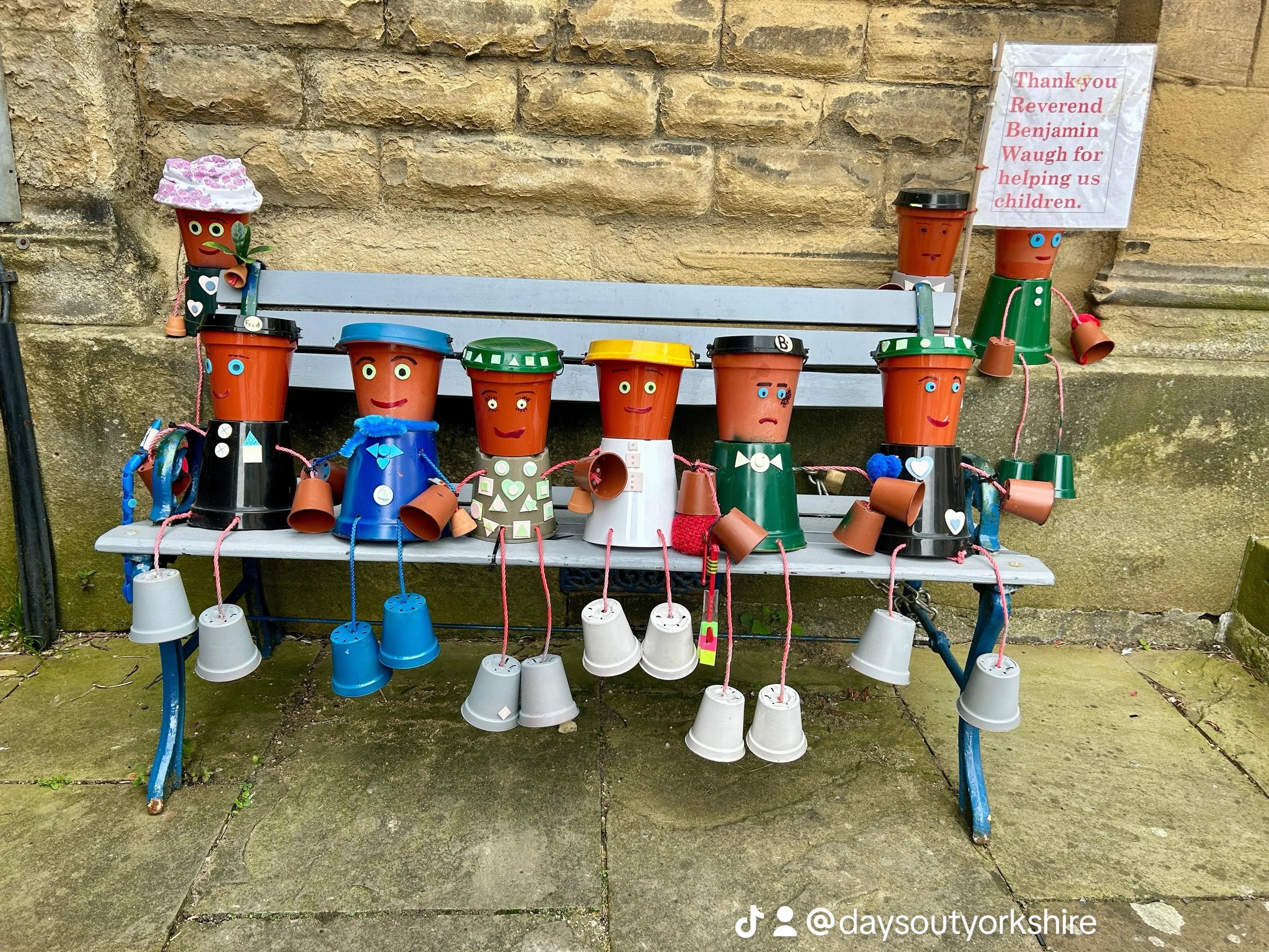 Row of little flowerpot people sitting on a bench in Settle, Yorkshire Dales, part of the annual Settle Flowerpot Festival