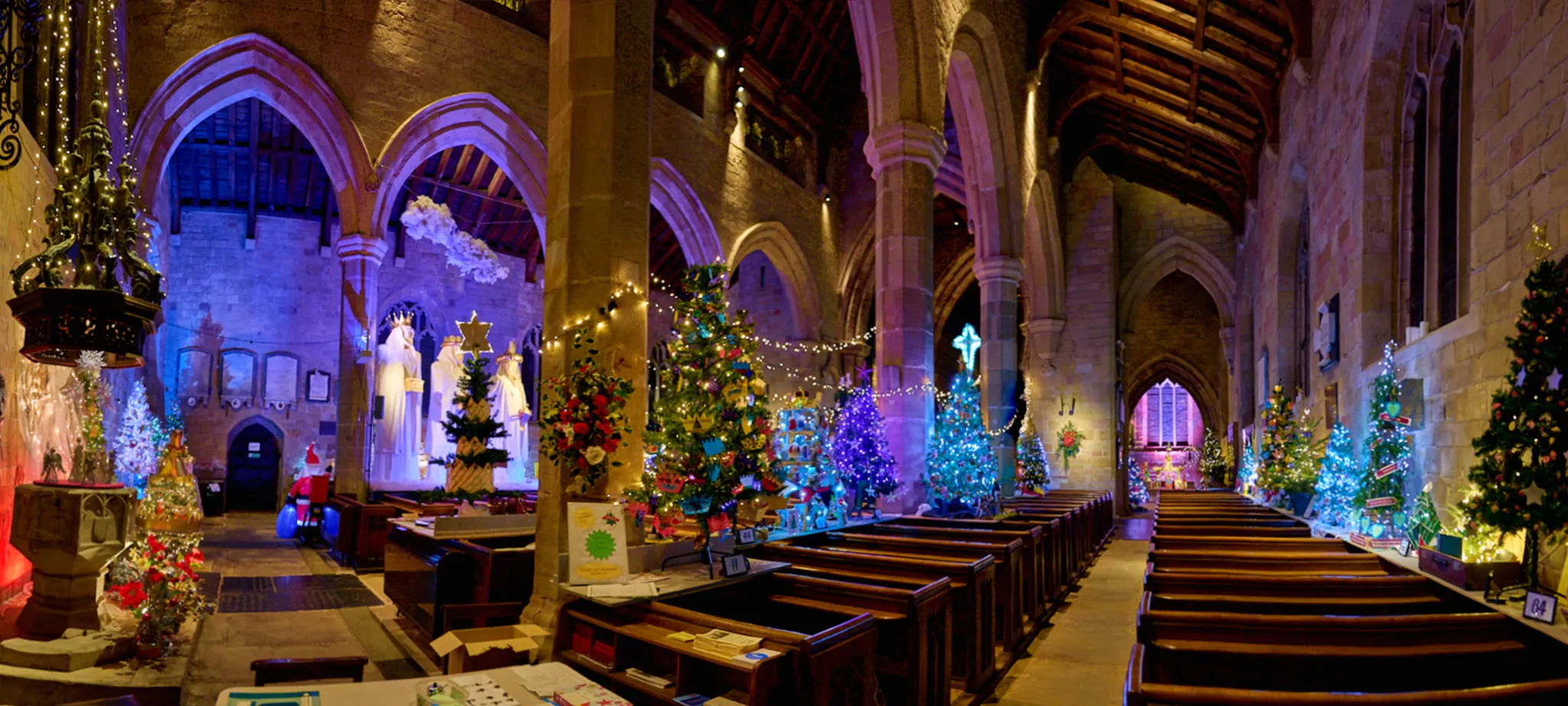 wide angle interior of st johns church in k'boro with rows of pews and the christmas tree festival trees