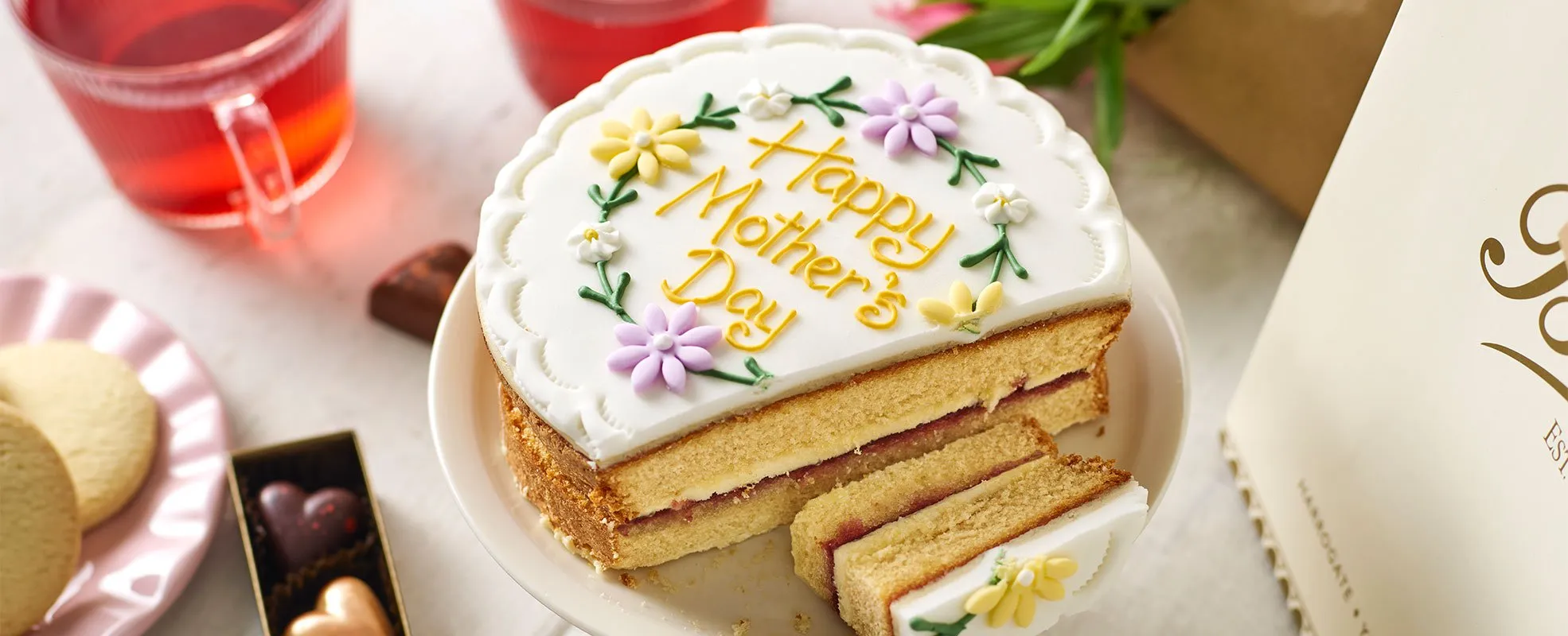 Betty's cake with white icing and words happy mothers day in yellow icing. 