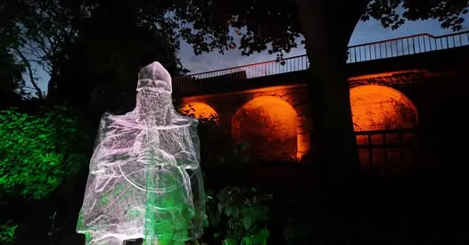 wire mesh scultpure of a night with a viaduct lit in the background