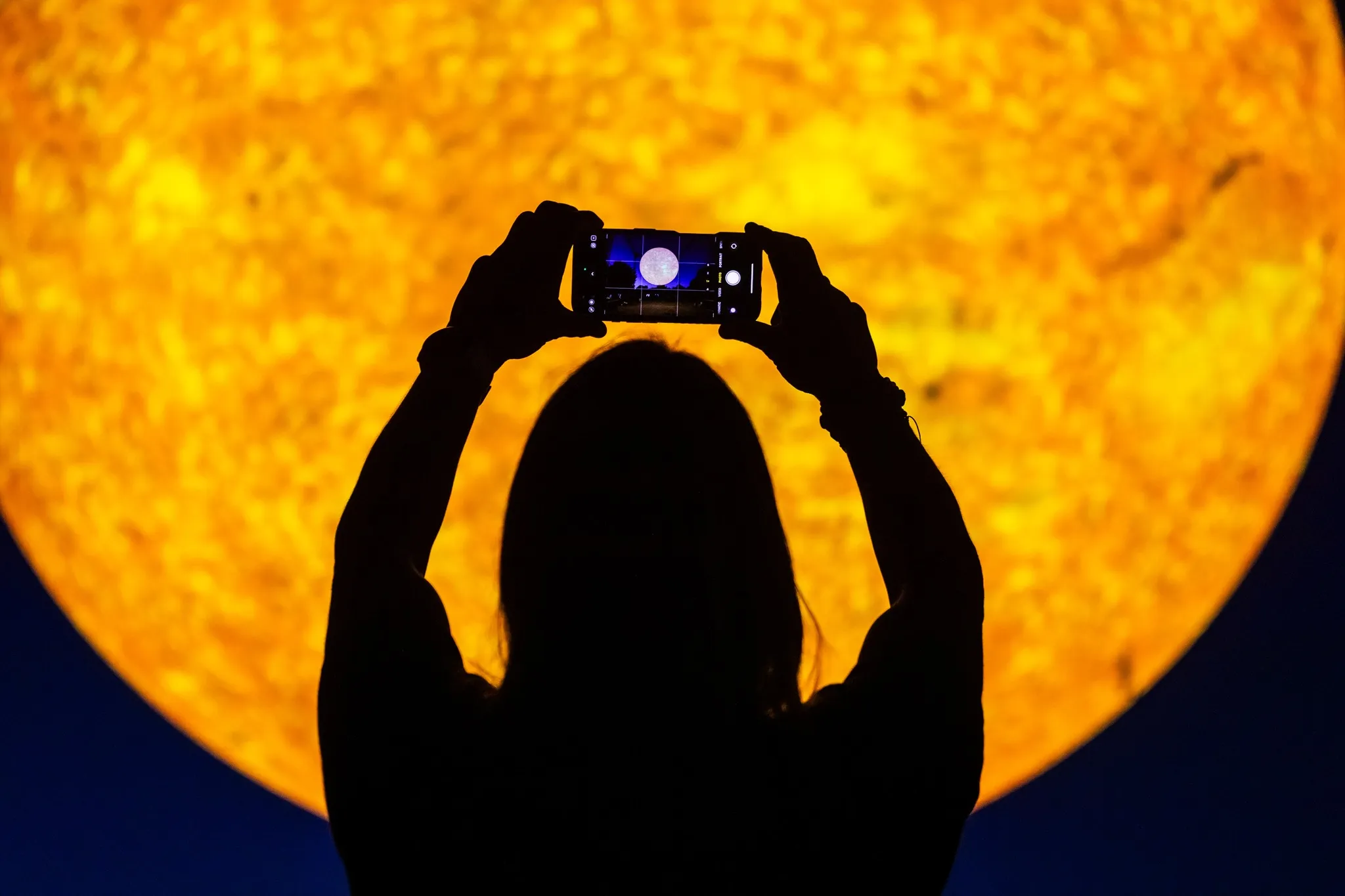 person silhouetted holding up a camers to the Helios sculpture