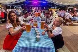 beer hall with people in bavarian style costumes seated at a table raising steins of beer